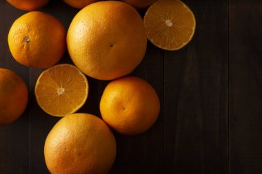 Olgunlaşmış portakal kesiminin düz bir görüntüsü ve kahverengi kırsal ahşap masa üzerinde fotokopi alanı olan bir sürü portakal.