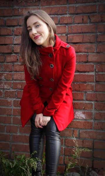 Beautiful girl in a red coat on brick wall background