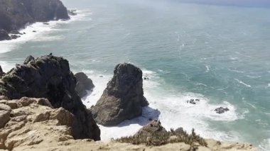 Güçlü okyanus dalgaları olan engebeli kıyı kayalarının panoramik görüntüsü doğa klipleri, seyahat görüntüleri veya dramatik deniz manzaraları için çarpışıyor..