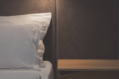 Temiz beyaz yastık ve çarşafları güzelce yapılmış bir otel yatağına yakın çekim. Minimalist tasarım ve hafif ışıklandırma bir rahatlık, sakinlik ve modern konukseverlik hissi yaratır..