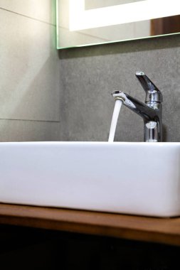 Modern banyo lavabosu krom musluktan akan suyla dolu. Minimalist iç tasarım, temiz fayanslar ve yumuşak ışıklandırma, hijyen ve günlük kişisel bakım rutini..