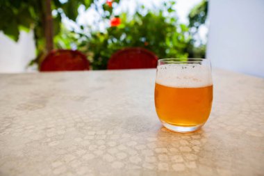 Yaz masasında, ılık güneş ışığında parlayan bir bardak soğuk light bira. Ferahlatıcı mevsimlik içki sahnesi rahatlama, rahatlama ve açık hava yaz atmosferi için mükemmel..