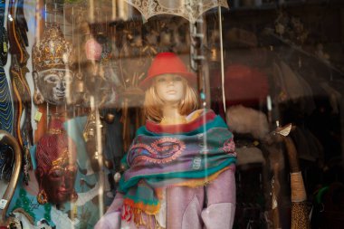 Etnik kıyafetler, maskeler, eşarplar, mücevherler ve kırmızı şapkalı ve desenli atkılı bir manken vitrininde canlı el yapımı aksesuarlar sergileniyor..