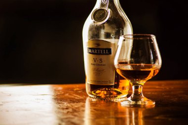 Fransız Martell vs Single Distillery konyak şişesi koyu siyah arka planda dolu bir bardakla. Yakın çekim, zarif atmosfer, yeni yıl ve kış tatili teması için mükemmel..