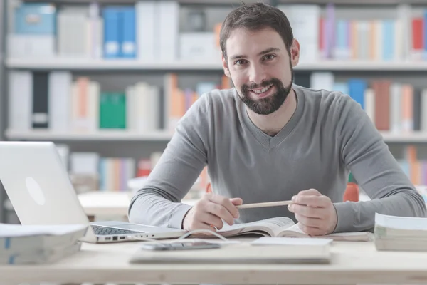 Uomo che legge un libro e usa un computer portatile — Foto Stock