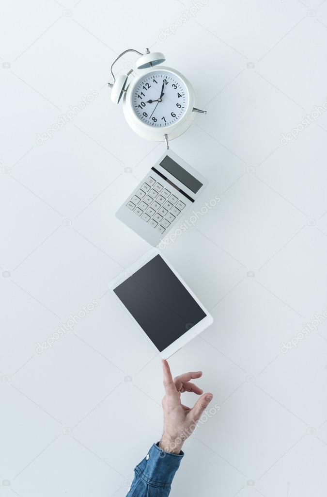 Casual businessman balancing a clock, a calculator and a digital tablet