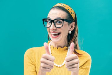 Neşeli, klasik tarzda bir kadın başparmağını kaldırıp kameraya gülümsüyor.