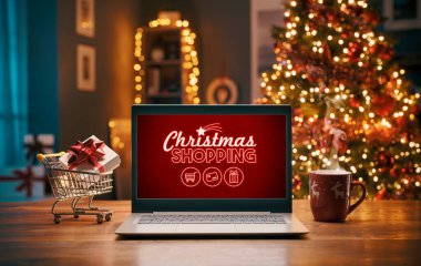 Evde Noel alışverişi, dizüstü bilgisayar ve içinde hediye olan minyatür alışveriş arabası, tatiller ve satış konsepti.