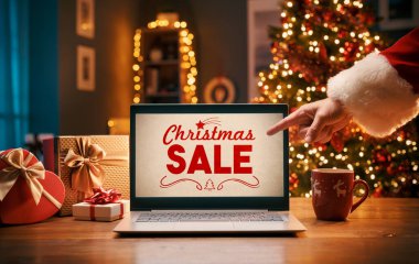 Noel Baba dizüstü bilgisayarında Noel reklamları gösteriyor. Bilgisayar ekranını işaret ediyor.