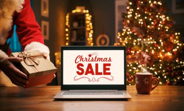 Noel Baba eve bir hediye ve dizüstü bilgisayarla Noel alışveriş reklamı getiriyor.