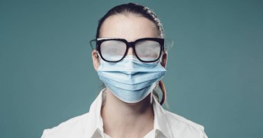 Koronavirüsü önlemek için koruyucu bir maske takan kadının gözlüğü buğulanmış.