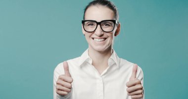 Neşeli başarılı iş kadını kameraya gülümsüyor ve başparmağını kaldırıyor.