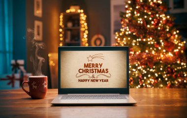 Dizüstü bilgisayarda Noel dilekleri ve arka planda ışıklar olan Noel ağacı.