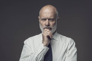 Çenesi, iş stratejileri ve liderlik konseptiyle düşünen kendinden emin orta yaşlı bir işadamının portresi.