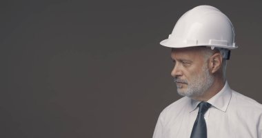 Kendine güvenen işadamı ve mühendis kaskla poz veriyor, kendi tarafına bakıyor.