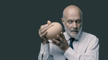 Kıdemli işadamı birikimlerini bir para kutusunda kontrol ediyor, sallıyor ve dinliyor, yatırım konsepti.