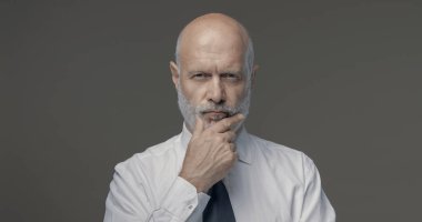 Çenesi, iş stratejileri ve liderlik konseptiyle düşünen kendinden emin orta yaşlı bir işadamının portresi.