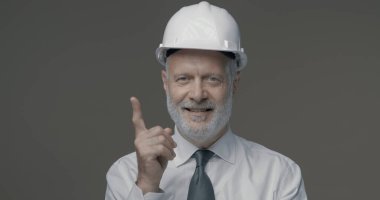 Neşeli iş adamı ve mühendis bir güvenlik kaskı takıyor ve yukarıya bakıyor.