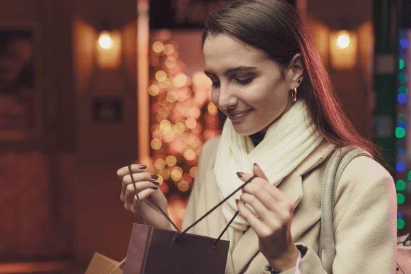 笑顔の女性は彼女のショッピングバッグをチェックし 彼女はクリスマスのために彼女の購入に満足しています — ストック写真