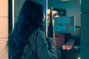 Coronavirus covid-19 salgını nedeniyle kapanan cerrahi maskeli bir kadın işareti okuyor.