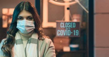 Coronavirus covid-19 salgını yüzünden dükkan kapalı. Maskeli bir kadın kameraya bakıyor.
