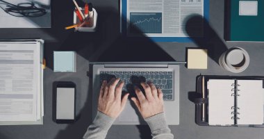 Corporate businessman working on a tidy organized desktop, he is typing on a laptop, top view
