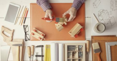 Creative craftsman and designer working at desk: he is painting a hand made wooden toy