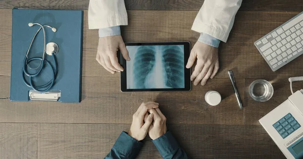 Doctor meeting a patient in the office and giving a medical consultation, he is using a digital tablet and checking medical records