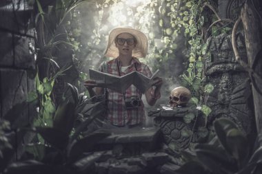 Ormanda kaybolan komik turist, elinde bir harita var ve antik harabelerin yanında duruyor.