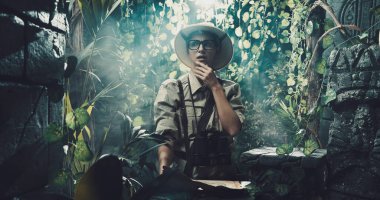 Korkak kâşif ormanda kayboldu. Elinde bir harita var ve eski kalıntılara bakıyor.