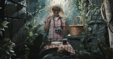 Tropikal bir ormanda piknik yapan mutlu bir turist eski harabelerin üzerine masa örtüsü örttü.