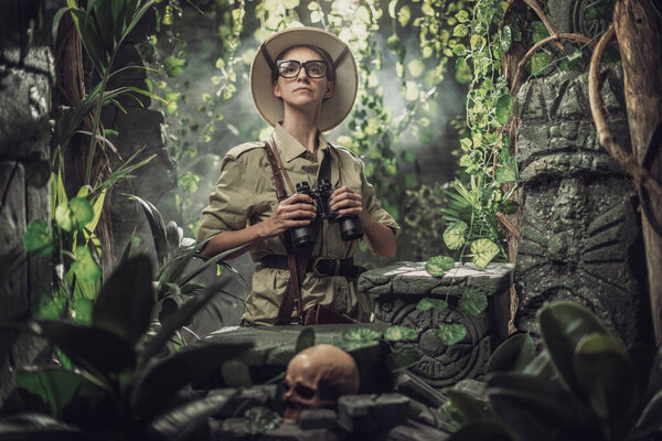 Brave woman exploring the tropical jungle and finding ancient ruins, she is holding binoculars and looking around