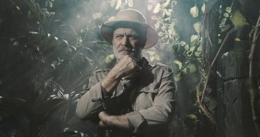 Tropikal ormanda cesur bir kâşif, eli çenesinde düşünüyor.