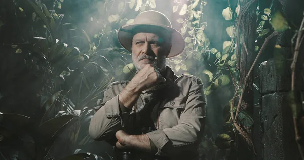 Tropikal ormanda cesur bir kâşif, eli çenesinde düşünüyor.