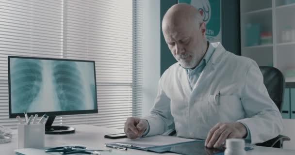 Профессиональный врач проверяет медицинские записи в своем кабинете — стоковое видео