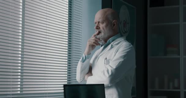 Pensionär läkare som står bredvid ett fönster — Stockvideo