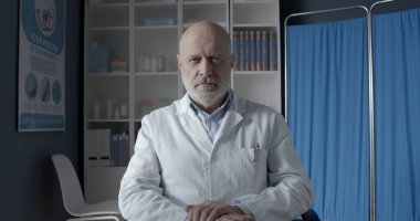 Profesyonel doktor ofis masasında oturuyor ve kameraya bakıyor, sağlık uzmanları