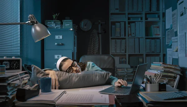 Exhausted young office worker sleeping at her desk, job burnout and overtime work concept