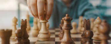 Çocuk satranç oynuyor ve bir taşı hareket ettiriyor, eli yakın.