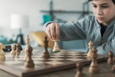 Evde satranç oynayan zeki çocuk, satranç tahtasının bir parçasını hareket ettiriyor.