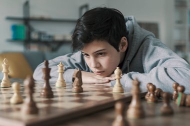Evde satranç oynayan akıllı çocuk, düşünüyor ve satranç tahtasına bakıyor.