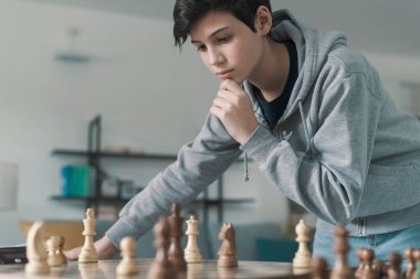 Evde satranç oynayan kendinden emin bir çocuk. Satranç tahtasındaki taşlara bakıyor ve düşünüyor. Strateji oyunları.