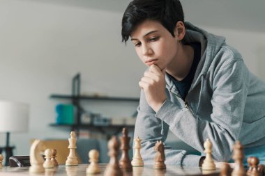 Evde satranç oynayan kendinden emin bir çocuk. Satranç tahtasındaki taşlara bakıyor ve düşünüyor. Strateji oyunları.