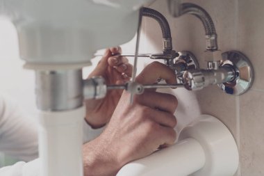 Profesyonel tesisatçı evdeki lavaboyu tamir ediyor. Boruları ingiliz anahtarıyla kontrol ediyor.