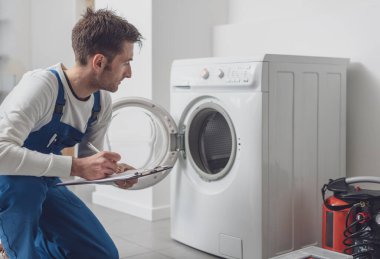 Profesyonel teknisyen çamaşır makinesini kontrol ediyor. Panoya yazı yazıyor.