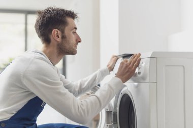 Tamirci çamaşır makinesini tamir ediyor. Kontrol panelinin düğmesini ayarlıyor.