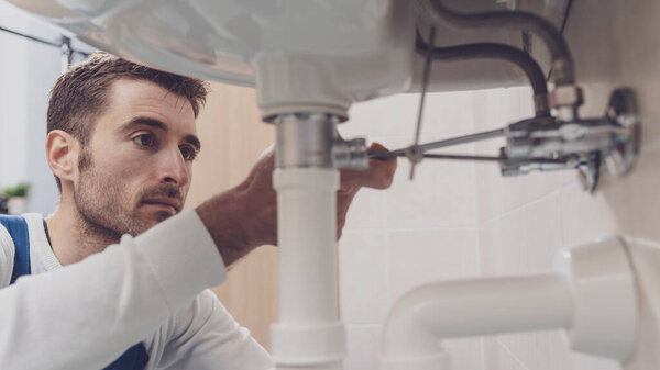 Профессиональный сантехник чинит раковину дома, проверяет трубы гаечным ключом