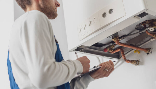 Professional plumber servicing a boiler and writing on a clipboard