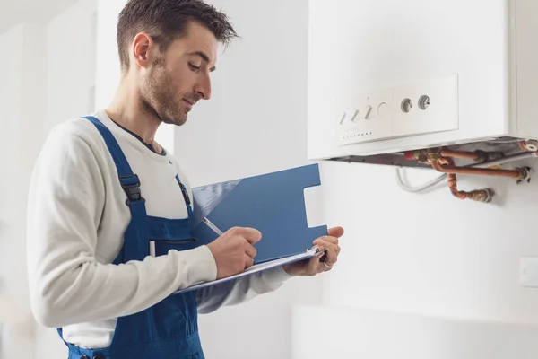 Professional plumber checking a boiler at home and writing on a clipboard