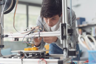 Akıllı genç öğrenci 3D baskı öğreniyor, yazıcıyı kontrol ediyor.
